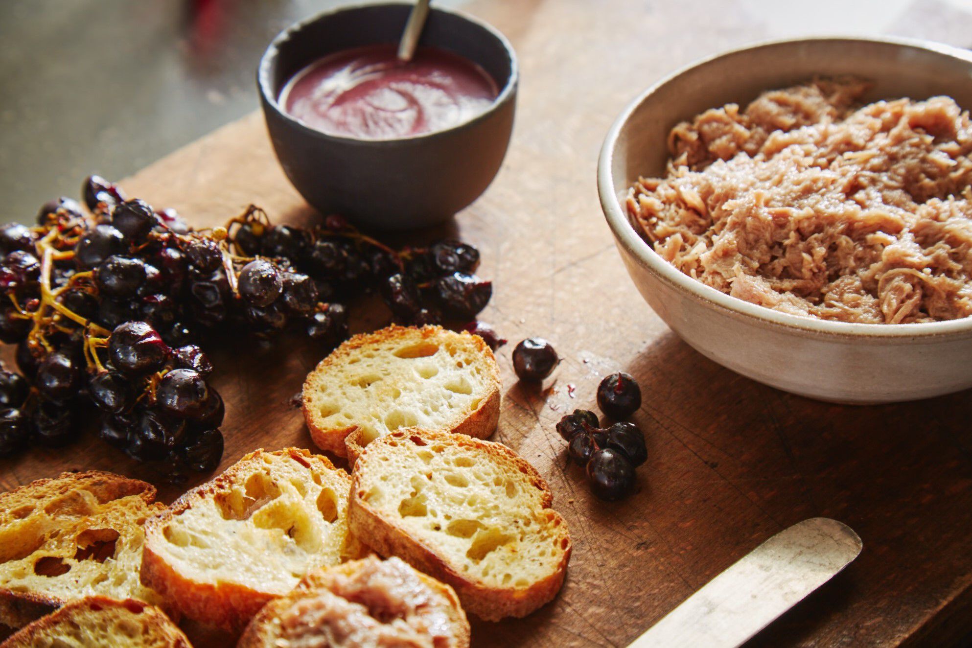 Grapes and bread on a cutting board with duck rillettes.